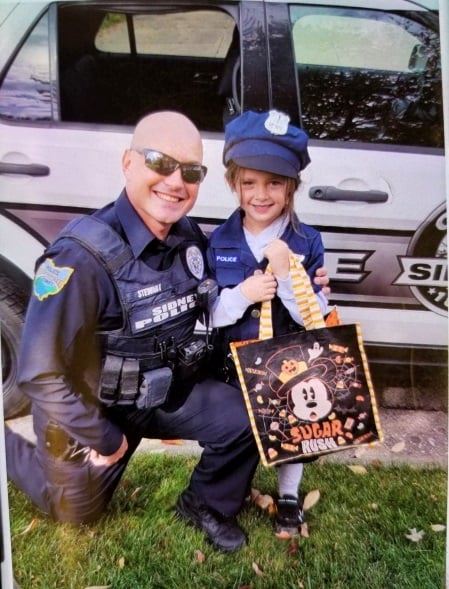 Community Resource officer poses in front of cruiser with a child 